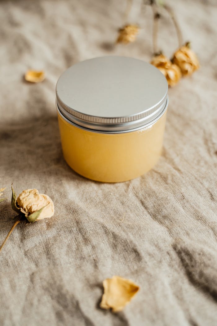Eco-friendly body butter container on rustic fabric with dried flowers.